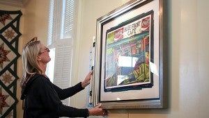 ON THE LEVEL: H.C. Porter hangs up a portrait of blues artist Jimmy Duck Holmes Monday in Main Street Market as part of her Blues @ Home: Mississippi’s Living Blues Legends show. (Justin Sellers/The Vicksburg Post)